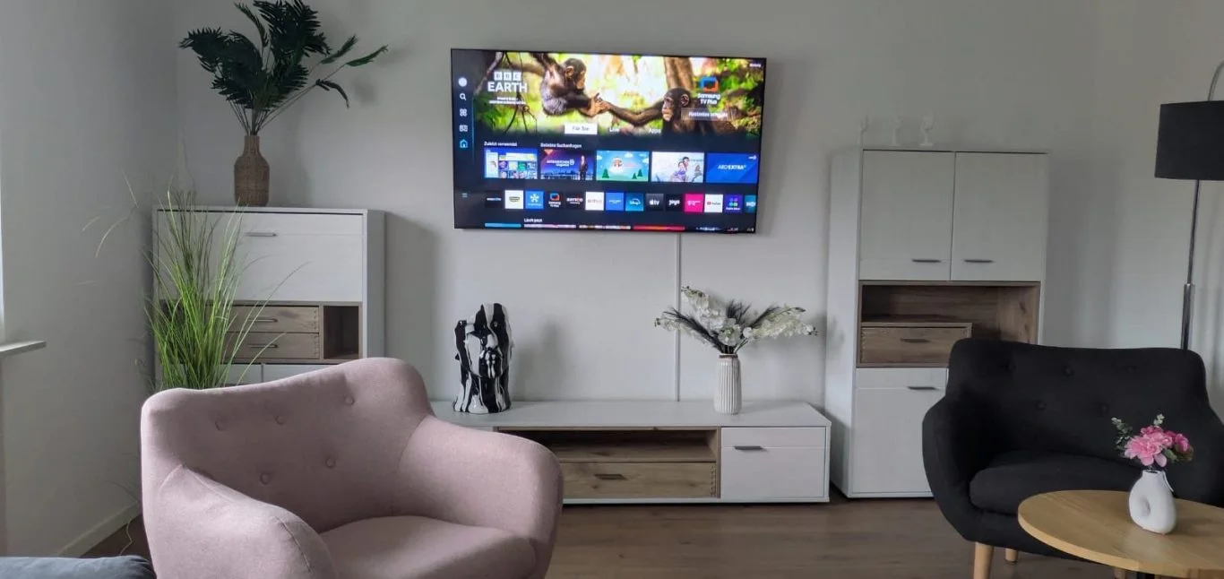 Wohnbereich bei FEWOHOME mit Fernseher, Sesseln und Wohnzimmerschränken